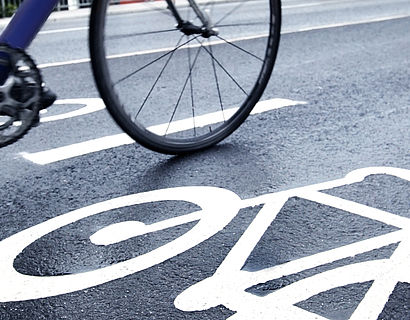Asphaltierte Straße mit Fahrradsymbol und Radfahrenden, die vorbeifahren