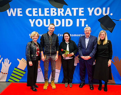 Gratulant*innen und eine Absolventin bei einem Gruppenfoto