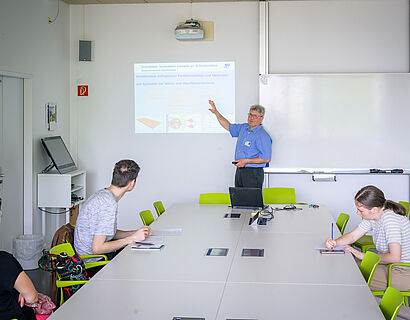Mitarbeiter der TH Wildau erklärt Besucherinnen und Besuchern etwas am Whiteboard.