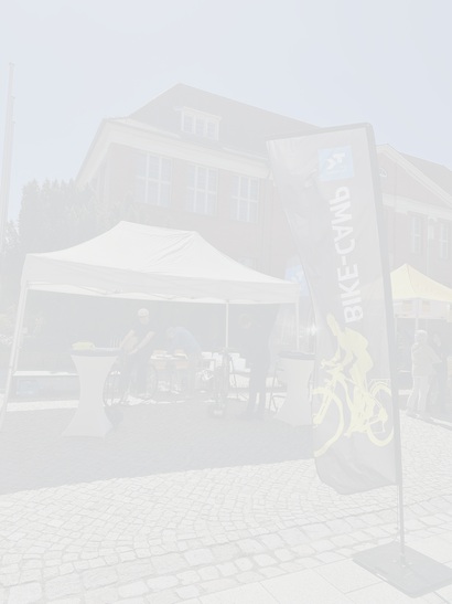 Bike-Coaching-Stand mit Zelt auf einem Campusplatz; mehrere Personen überprüfen und justieren Fahrräder, daneben eine Fahne mit „Bike-Camp“ und TK-Logo.