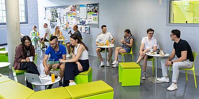 Studierende in kleinen Gruppen an unterschiedlichen Tischen im Café von Halle 17 im Gespräch