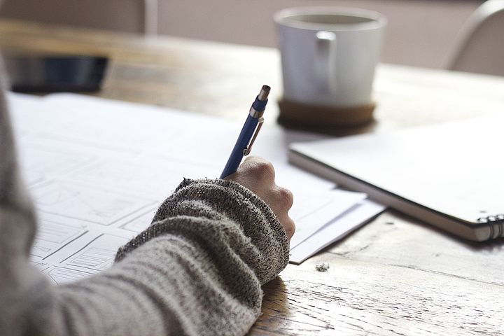 Schreibende Hand, Tasse und ein Heft im Hintergrund