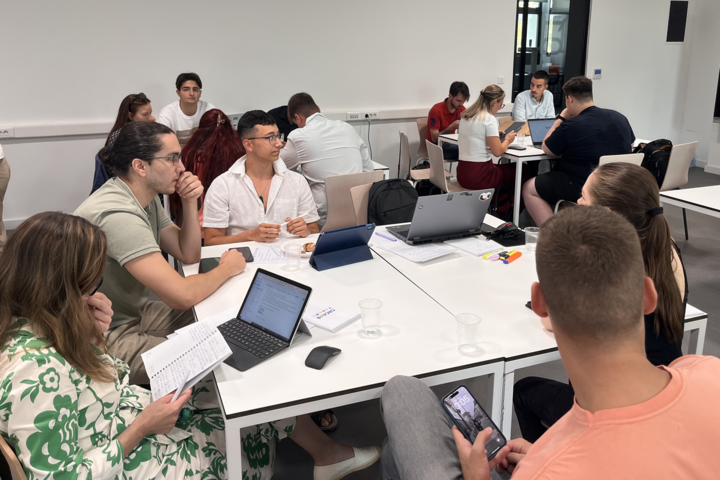 Studierende sitzen an Tischen und arbeiten an Laptops