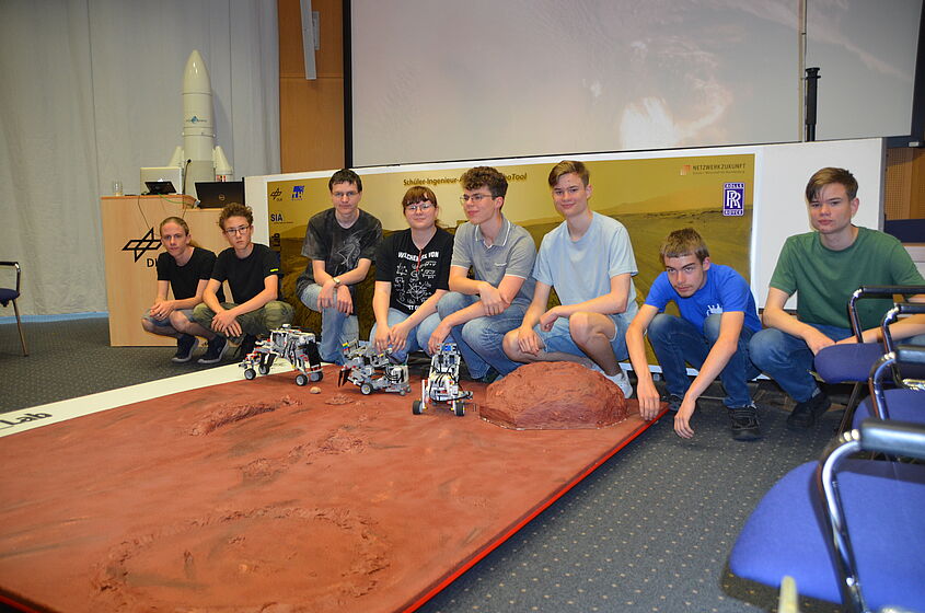 Schüler-Ingenieur-Akademie Kinder sitzen in einer Reihe vor einer nachempfundenen künstlichen Marslandschaft mit kleinen Marsrobotern