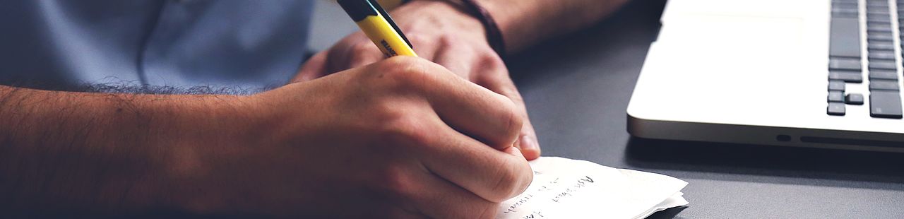 Mann sitzt am Schreibtisch mit seinem Laptop und schreibt Notizen