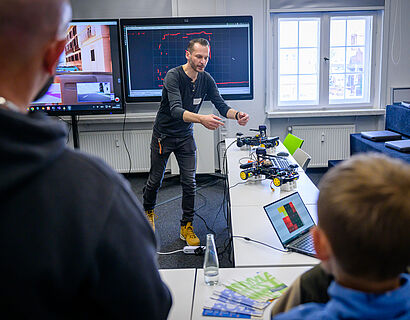 Prof. Stefan Kubica erklärt im Future Mobility Center ein Modellauto, im Vordergrund zwei Personen 