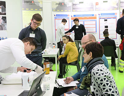 Schülerinnen und Schüler sowie Gäste beim Wettbewerb "Jugend forscht" an einem Ausstellungstisch