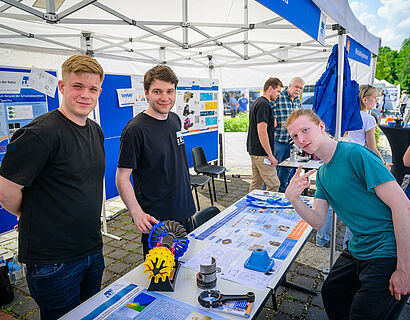 Studierende am Stand auf dem Campus der TH Wildau lächeln in die Kamera.