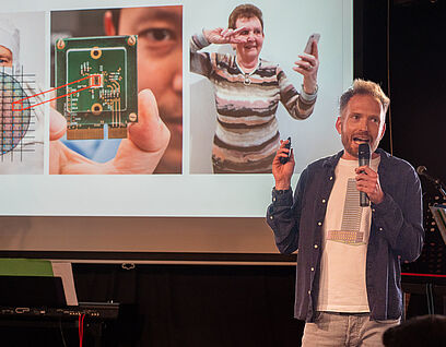 Mann steht mit einem Mikrofon in der Hand auf einer Bühne und hält eine Präsentation beim Brandenburger Science Slam 2025