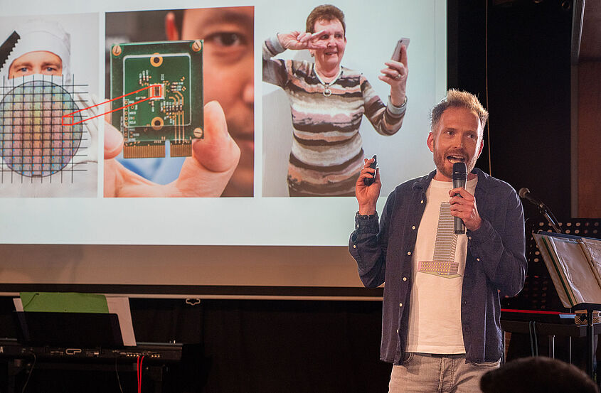 Mann steht mit einem Mikrofon in der Hand auf einer Bühne und hält eine Präsentation beim Brandenburger Science Slam 2025