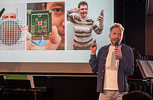 Mann steht mit einem Mikrofon in der Hand auf einer Bühne und hält eine Präsentation beim Brandenburger Science Slam 2025