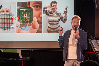 Mann steht mit einem Mikrofon in der Hand auf einer Bühne und hält eine Präsentation beim Brandenburger Science Slam 2025