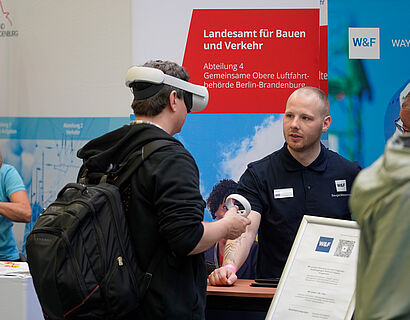 Aussteller im Gespräch mit einem Studierendem, der eine VR-Brille trägt am Stand bei der THCONNECT 2025