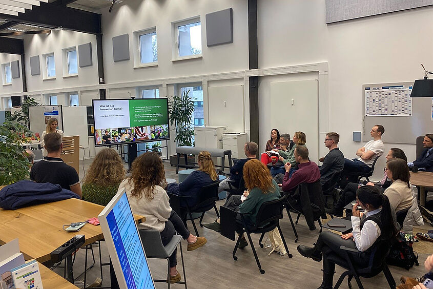 Personen sitzen auf Stühlen im Opp:Lab und verfolgen einen Vortrag