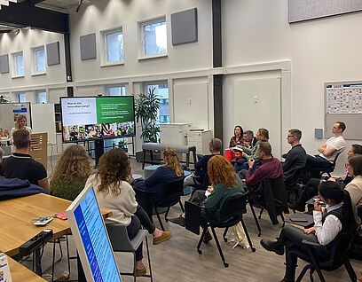 Personen sitzen auf Stühlen im Opp:Lab und verfolgen einen Vortrag