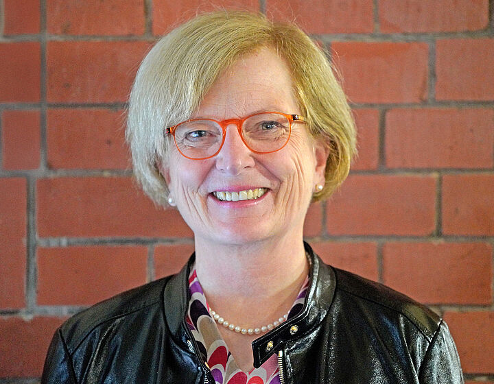 Portraitbild von Prof. Ulrike Tippe vor einer roten Backsteinwand