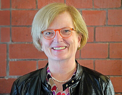 Portraitbild von Prof. Ulrike Tippe vor einer roten Backsteinwand