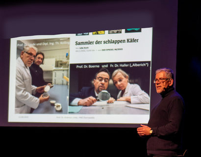 Brandenburger Science Slam Mann bei einem Vortrag mit einer Präsentation im Hintergrund