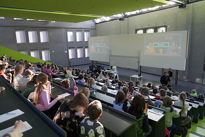 Kinder in einem voll besetzten Audimax von hinten fotografiert