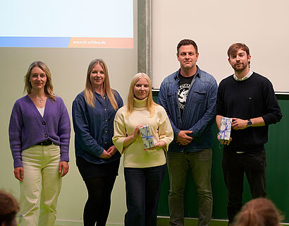 Gruppenbild der Teilnehmer*innen und Organisator*innen des THtalk, 5 Personen stehen in einem Hörsaal vor einer Tafel