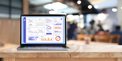 Laptop mit einem Dashboard auf einer Tischplatte mit verschwommenen Personen im Hintergrund
