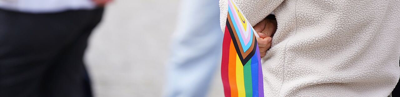 Nahaufnahme einer kleinen inter-inclusive Regenbogenflagge, die von einer Person in der Hand gehalten wird.