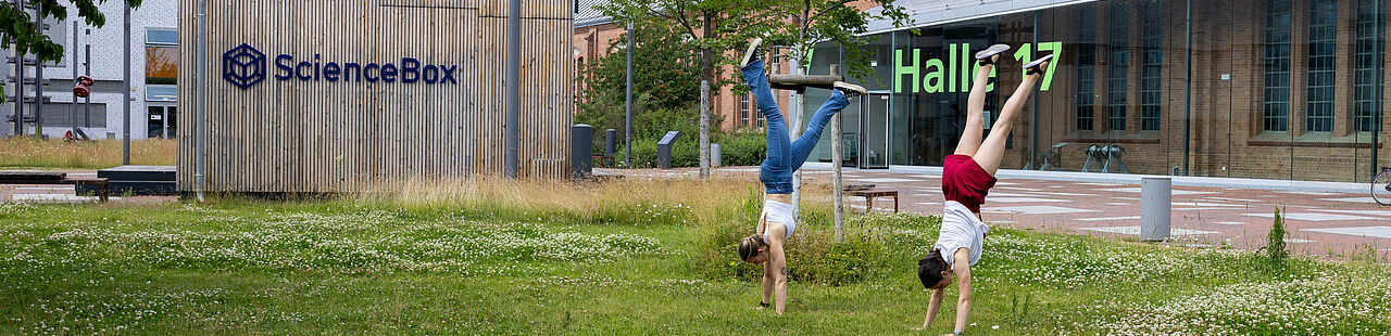 Zwei Studierende machen Handstand auf der Wiese vor Haus 16 auf dem Campus der TH Wildau