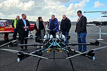 Personen stehen in einer Gruppe zusammen und unterhalten sich, im Vordergrund ist eine große Drohne zu sehen