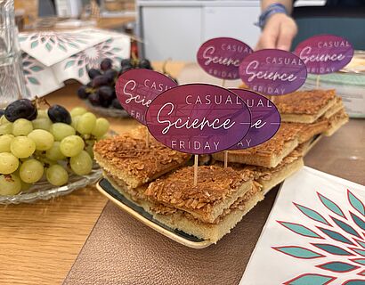 In dem Bild ist ein Bienenstichkuchen zu sehen mit kleinen lila pinken Schildchen wo "Casual Science Friday" draufsteht.