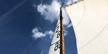 Blick auf den Segelmast eines Boots mit blauem Himmel und Wolken im Hintergrund
