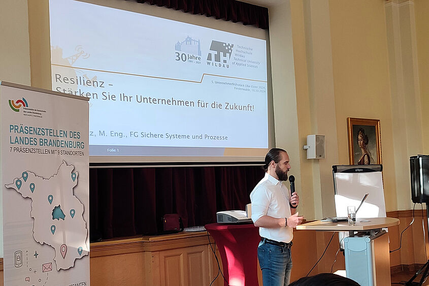 Resilienz Jan Seitz bei einem Vortrag an einem Rednerpult mit einer Präsentation im Hintergrund.