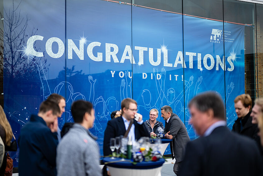 Absolvent/-innenverabschiedung 2022 Absolventinnen und Absolventen vor dem Banner in Halle 17 bei der Verabschiedung 2022