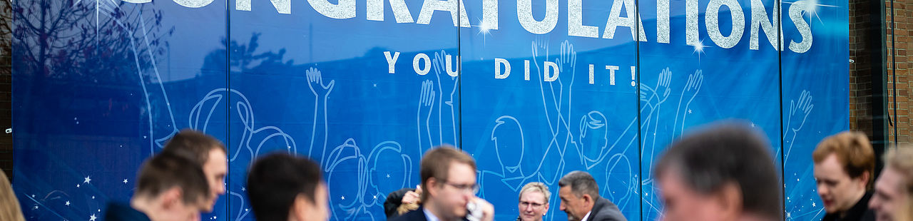 Absolventinnen und Absolventen vor dem Banner in Halle 17 bei der Verabschiedung 2022