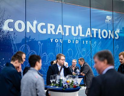 Absolventinnen und Absolventen vor dem Banner in Halle 17 bei der Verabschiedung 2022