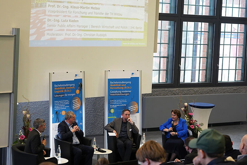 Personen sitzen in einer Gesprächsrunde mit Roll-ups im Hintergrund