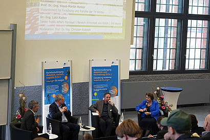 Personen sitzen in einer Gesprächsrunde mit Roll-ups im Hintergrund