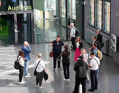 Gruppe steht im Rahmen einer Campustour im Foyer eines Hochschulgebäudes