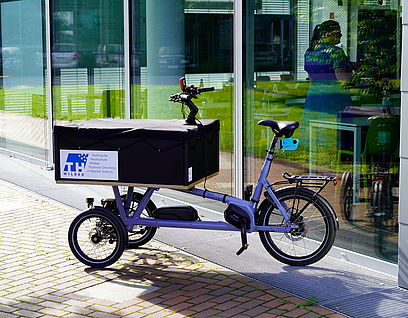Bild eines Lastenrads mit TH-Wildau-Logo vor Haus 16 auf dem Campus