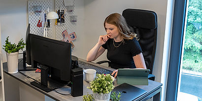 Studierende sitzt im Wohnheim am Schreibtisch vor dem PC und schaut sich etwas an