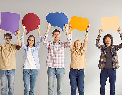 Fünf junge Menschen halten bunte Sprechblasen aus Papier in die Luft.