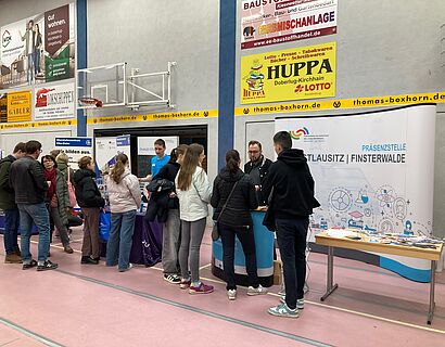 Zu sehen sind Menschen in einer Turnhalle an einem Stand der Karrieremesse