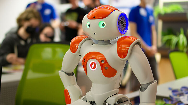 Humanoider Roboter auf einem Tisch mit Personen im Hintergrund