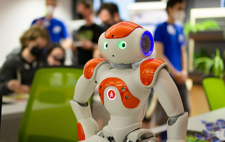 Humanoider Roboter auf einem Tisch mit Personen im Hintergrund