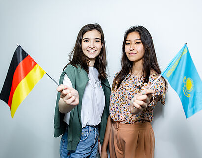 2 Studentinnen schwenken die deutsche und die kasachische Flagge