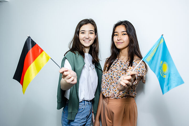 2 Studentinnen schwenken die deutsche und die kasachische Flagge