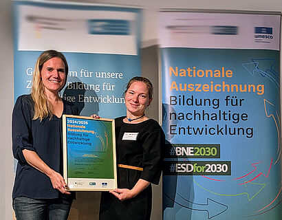 Zwei Frauen halten eine Urkunde in der Hand und lachen in die Kamera