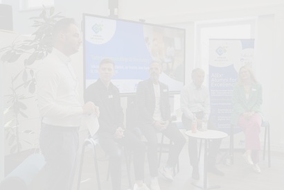 Auf dem Bild sind 5 Personen zu sehen, diese sitzen im Halbkreis vor einer elektrischen Tafel. Eine Person von ihnen steht, diese ist ganz links zu sehen und spricht in den Raum hinein.
