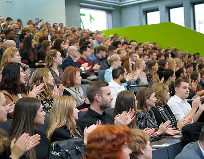 Gefülltes Audimax mit applaudierendem Publikum bei der feierlichen Verabschiedung der Absolventinnen und Absolventen 2023 des Fachbereichs WIR