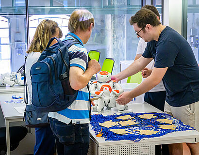 Besucherinnen und Besucher schauen sich in einem Labor einen humanoiden Roboter an. 