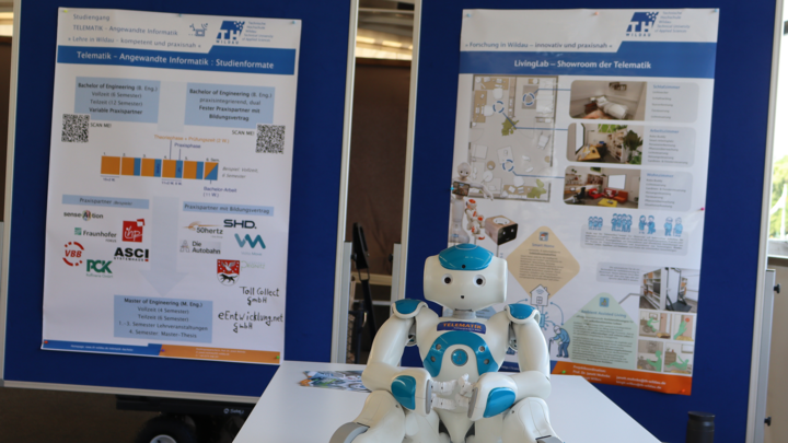 Humanoider Roboter NAO vor zwei Stellwänden mit Informationspostern